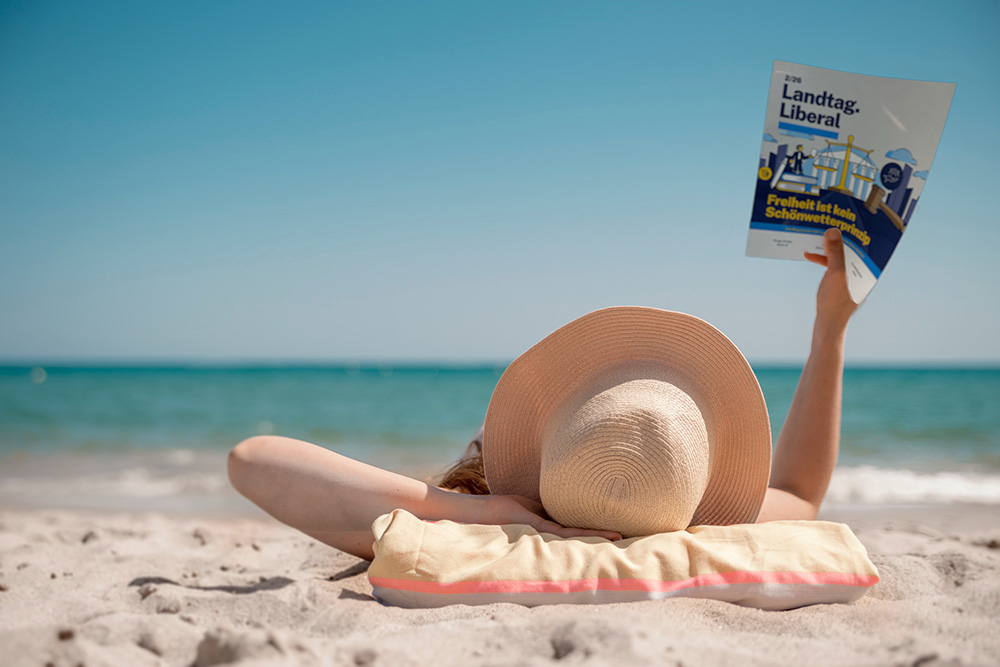 Eine Person am Strand liest das Magazin Landtag.Liberal