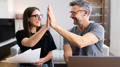 Frau mit Papieren in einer Hand gibt ihrem Mann ein High-Five