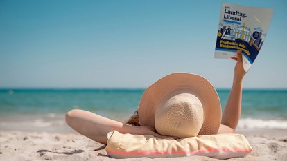 Eine Person am Strand liest das Magazin Landtag.Liberal