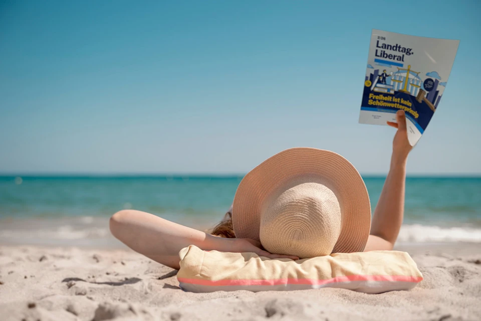 Eine Person am Strand liest das Magazin Landtag.Liberal